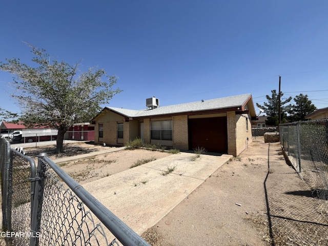 view of front facade featuring central AC unit, fence, concrete driveway, brick siding, and a garage