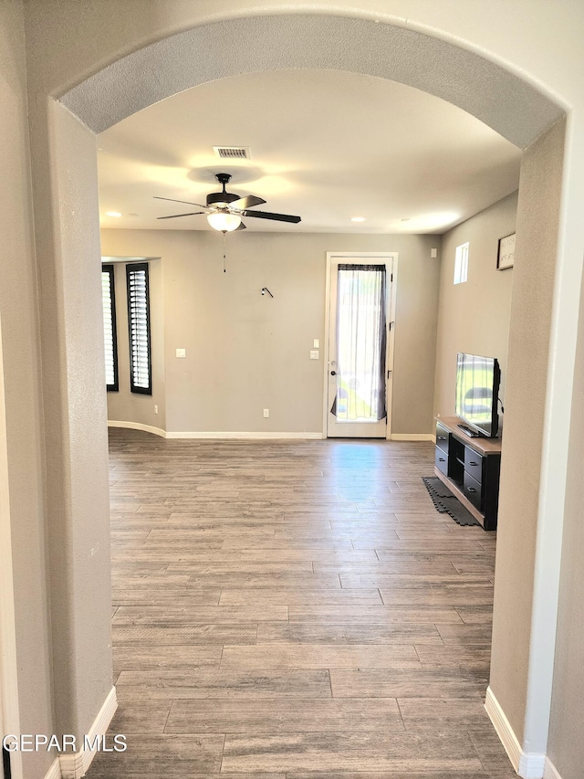 unfurnished living room with a ceiling fan, wood finished floors, plenty of natural light, and baseboards