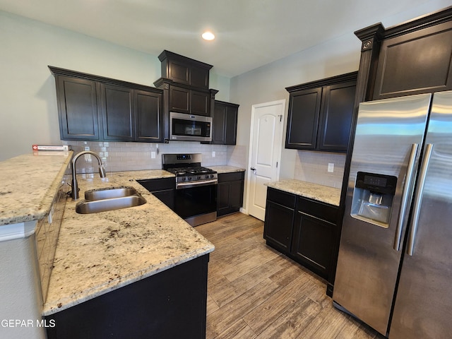 kitchen featuring stainless steel appliances, a sink, a peninsula, light stone counters, and light wood-style floors