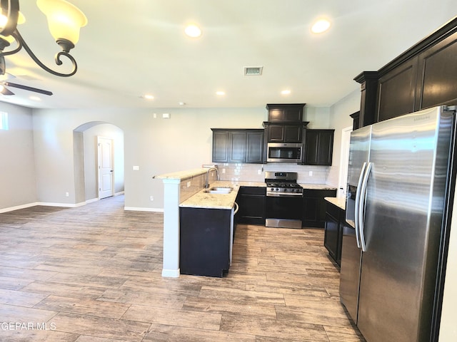 kitchen with appliances with stainless steel finishes, arched walkways, a sink, tasteful backsplash, and ceiling fan