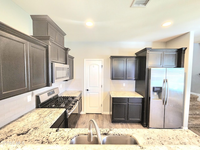 kitchen featuring appliances with stainless steel finishes, a sink, light stone countertops, tasteful backsplash, and recessed lighting