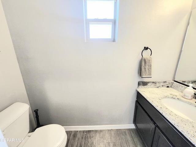 half bath featuring toilet, wood finished floors, baseboards, and vanity