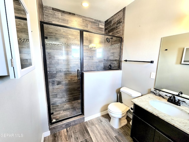 bathroom featuring a stall shower, toilet, vanity, wood finished floors, and baseboards