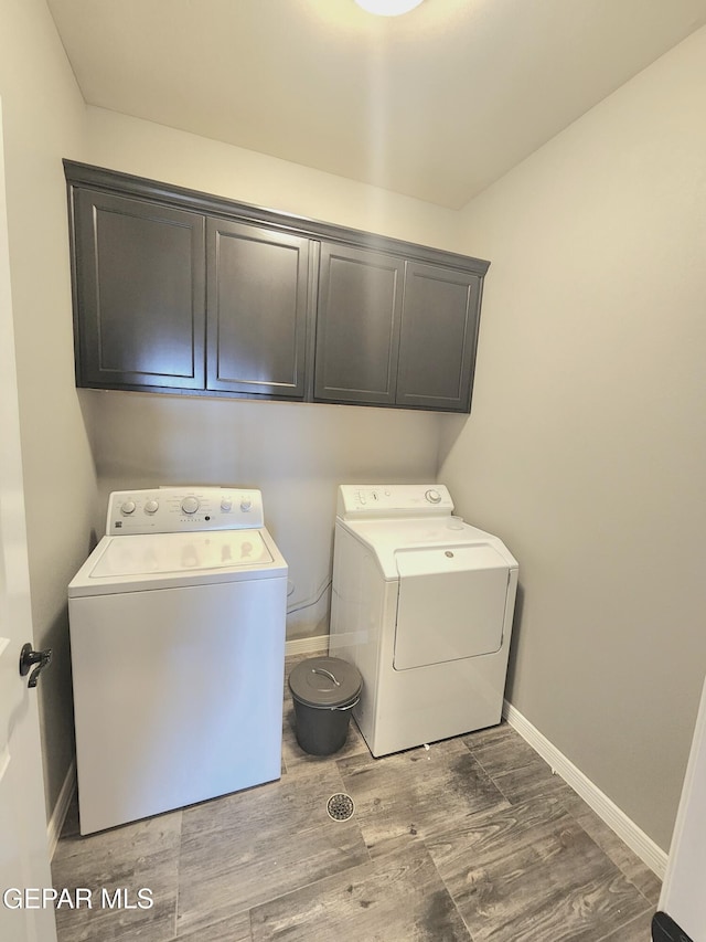 washroom with washer and clothes dryer, cabinet space, wood finished floors, and baseboards