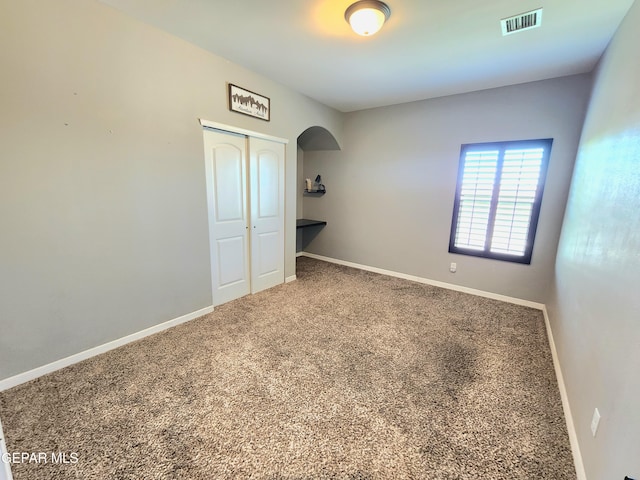empty room with arched walkways, carpet floors, and baseboards