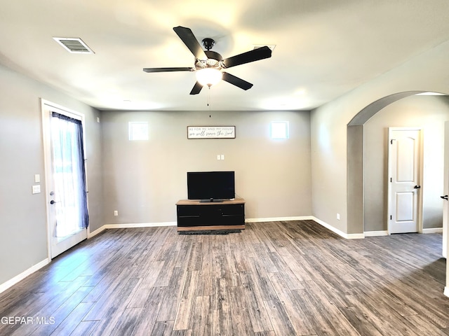 unfurnished living room with arched walkways, ceiling fan, wood finished floors, and baseboards