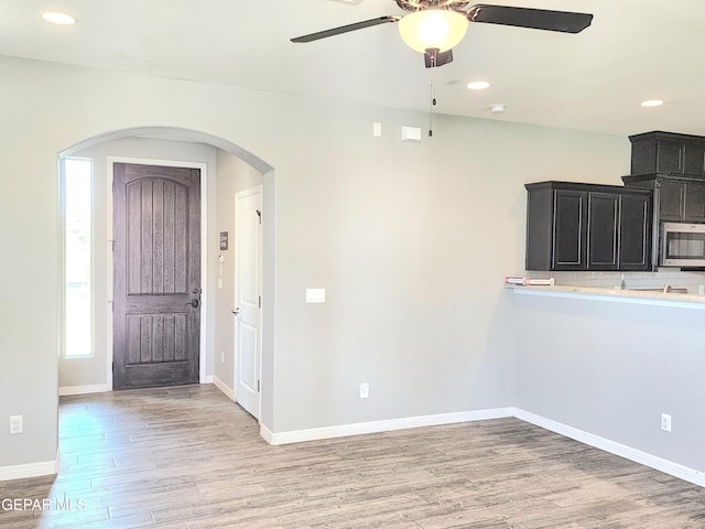 spare room with arched walkways, light wood finished floors, ceiling fan, recessed lighting, and baseboards