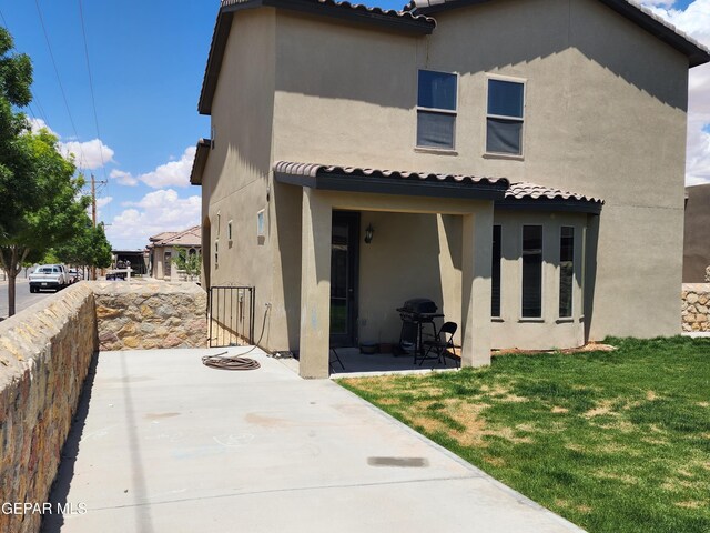 rear view of property featuring stucco siding, a tile roof, a patio area, and a lawn