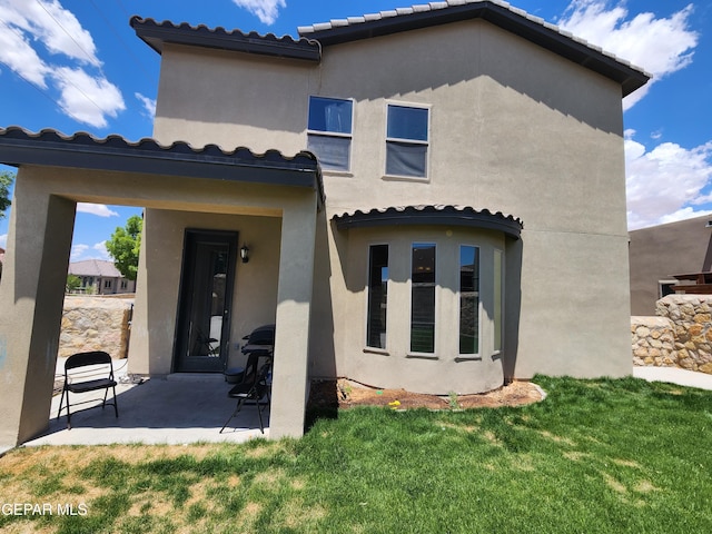 back of property with stucco siding, a yard, a patio, and a tile roof