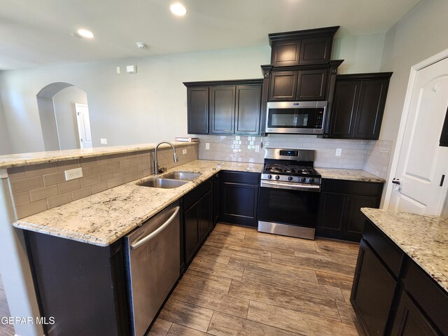 kitchen featuring stainless steel appliances, a sink, arched walkways, light stone counters, and tasteful backsplash