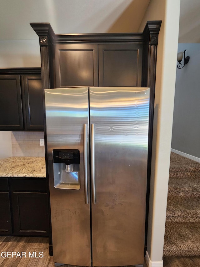 kitchen featuring stainless steel refrigerator with ice dispenser, decorative backsplash, light stone countertops, and baseboards