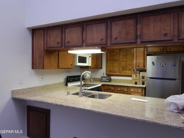 kitchen with a peninsula, a sink, freestanding refrigerator, white microwave, and electric stove
