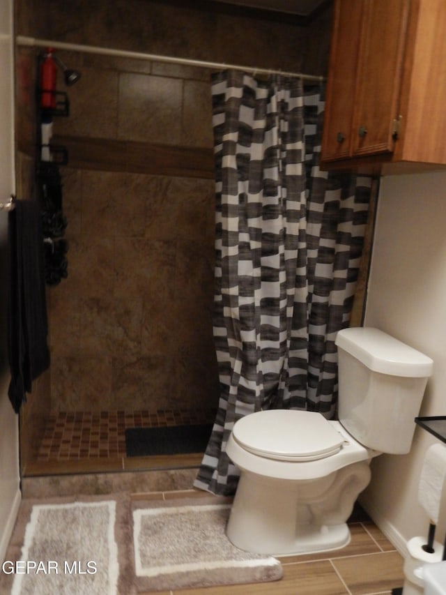 full bath featuring baseboards, toilet, and tiled shower