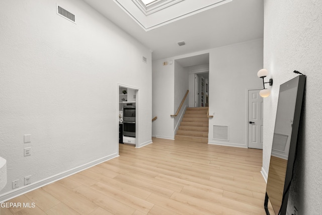 empty room with light wood-style floors, stairway, visible vents, and a skylight