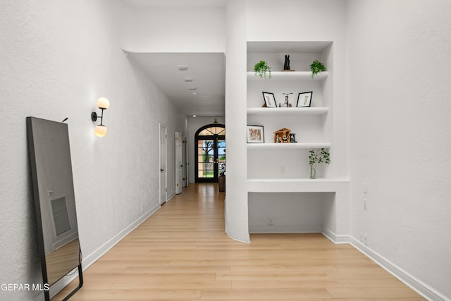 hall featuring light wood-style floors, visible vents, built in features, and baseboards