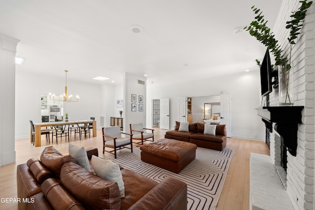living area featuring recessed lighting, a brick fireplace, light wood-style floors, and a chandelier