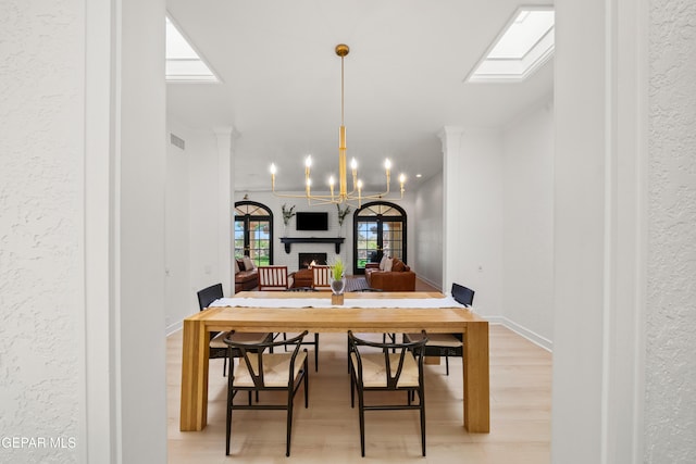 dining space featuring light wood-type flooring, visible vents, a notable chandelier, a skylight, and a textured wall