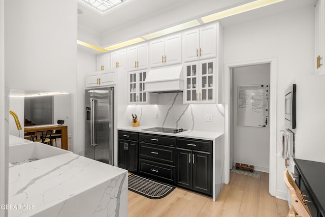 kitchen featuring white cabinets, stainless steel appliances, dark cabinetry, glass insert cabinets, and custom range hood