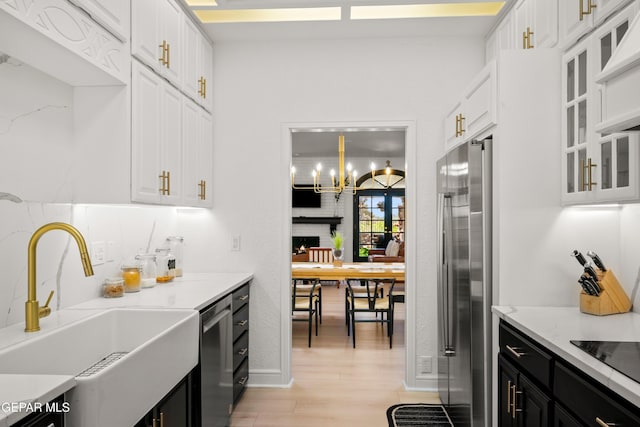kitchen featuring dark cabinets, a sink, light wood-style flooring, appliances with stainless steel finishes, and white cabinetry