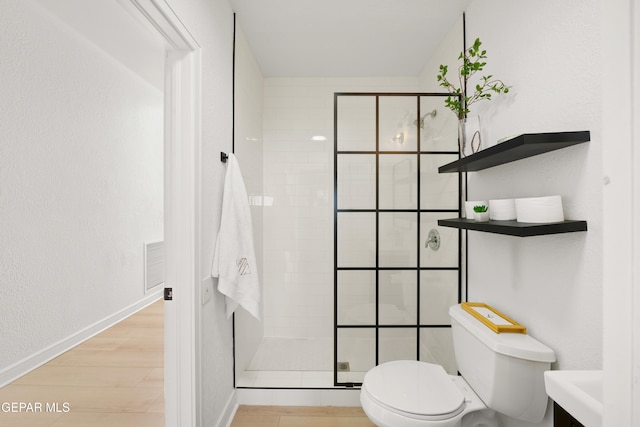 bathroom with wood finished floors, baseboards, a tile shower, toilet, and visible vents