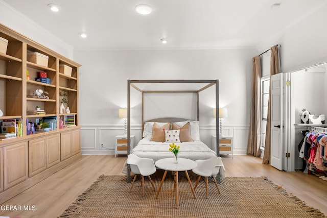bedroom with light wood-style flooring, a decorative wall, a wainscoted wall, and ornamental molding