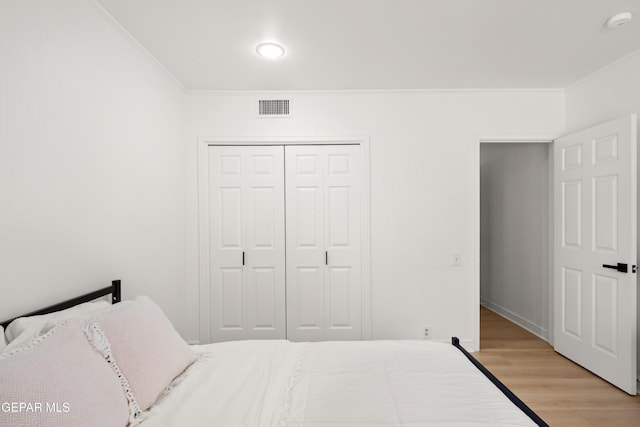 bedroom with ornamental molding, wood finished floors, visible vents, and a closet