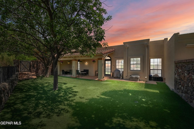 rear view of property featuring a yard, a patio area, stucco siding, and fence