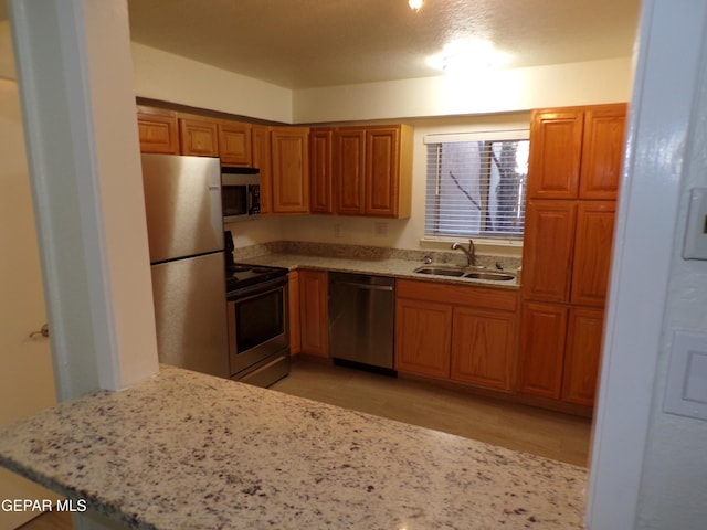 kitchen featuring light wood finished floors, a sink, light stone counters, brown cabinetry, and appliances with stainless steel finishes
