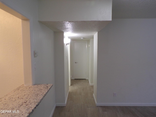 hallway with baseboards, wood finished floors, and a textured ceiling