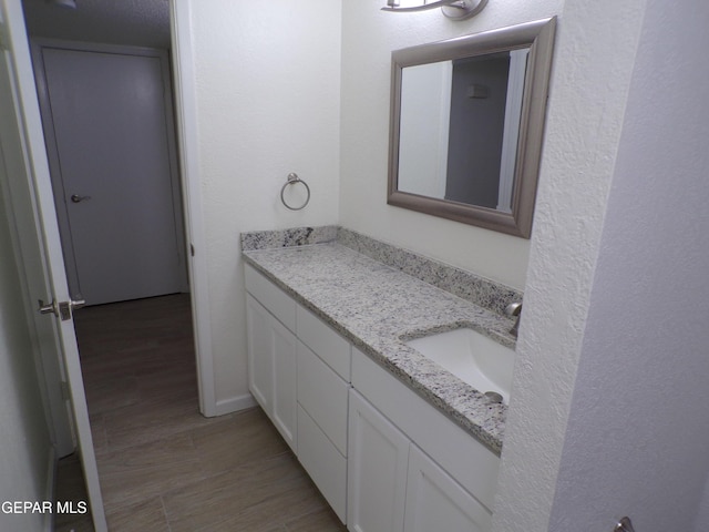 bathroom with a textured wall, vanity, and wood finished floors