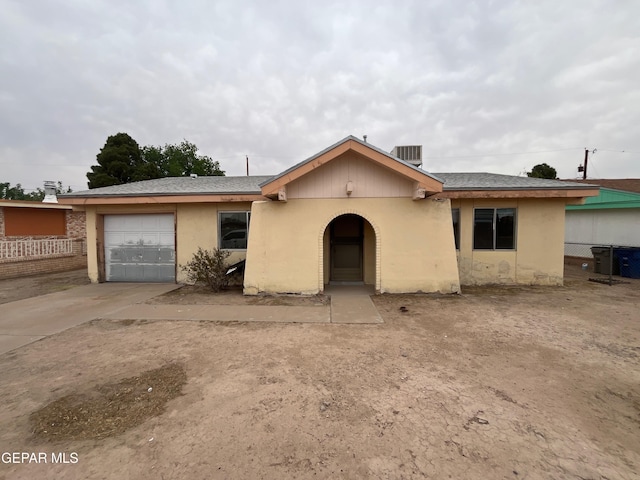 view of front of house with concrete driveway, central air condition unit, an attached garage, fence, and stucco siding