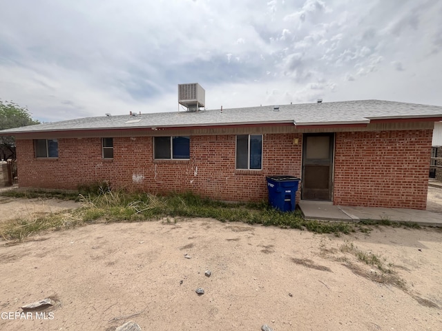 back of house featuring brick siding, roof with shingles, central AC, and a patio