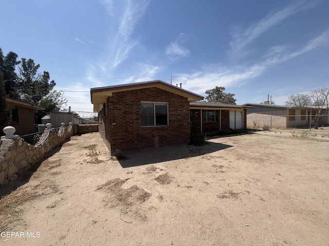back of house featuring brick siding, an attached garage, fence, and driveway