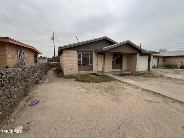 view of front of property featuring brick siding, an attached garage, driveway, and fence