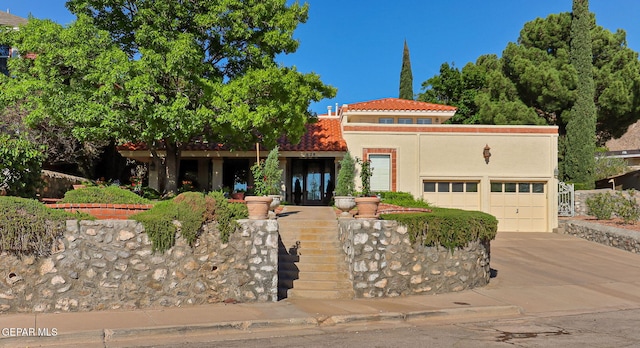 mediterranean / spanish house with a garage, stucco siding, stairs, a tiled roof, and concrete driveway