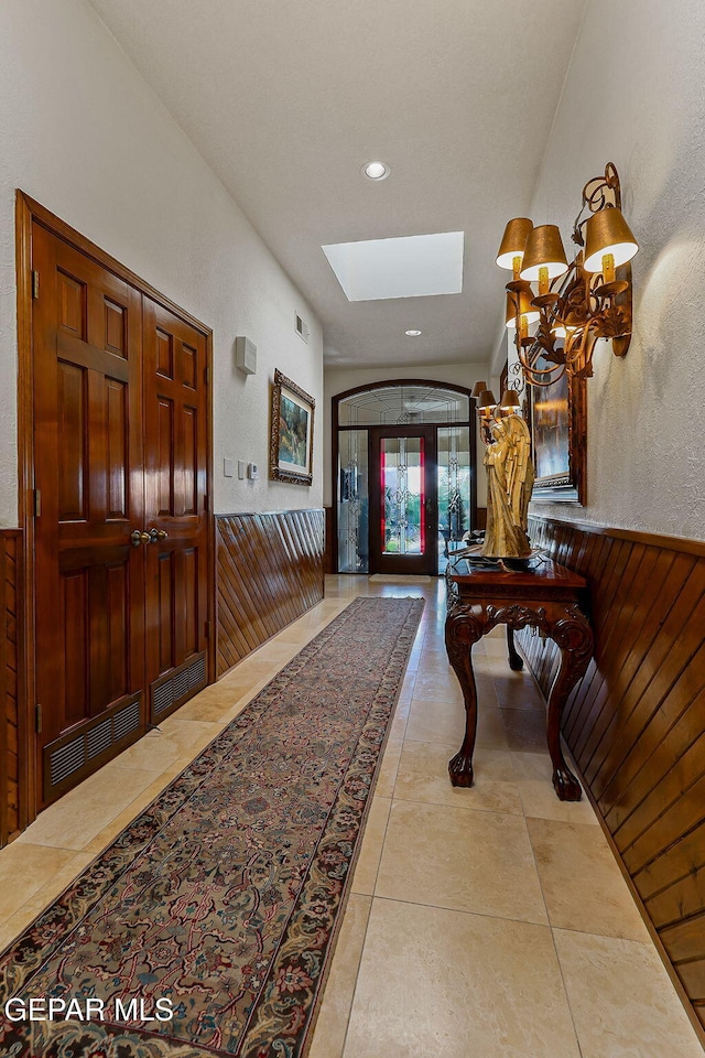 foyer entrance featuring a skylight, wainscoting, a notable chandelier, wooden walls, and recessed lighting