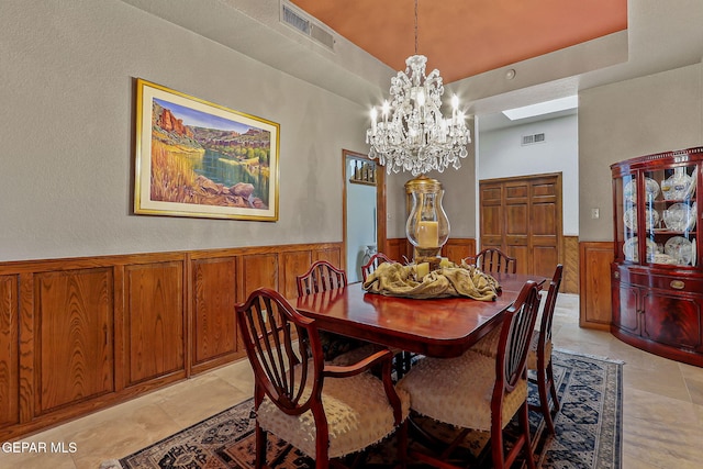 dining area with visible vents, wooden walls, a wainscoted wall, and a notable chandelier