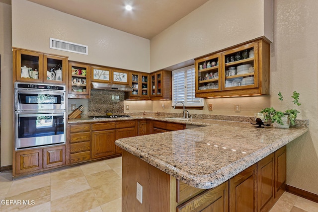 kitchen with appliances with stainless steel finishes, brown cabinetry, a peninsula, under cabinet range hood, and visible vents