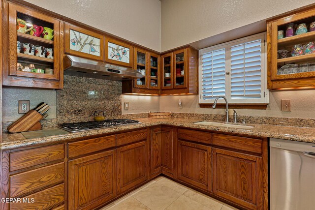 kitchen with backsplash, appliances with stainless steel finishes, a sink, a textured wall, and under cabinet range hood