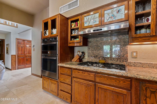 kitchen with decorative backsplash, brown cabinetry, visible vents, under cabinet range hood, and stainless steel appliances