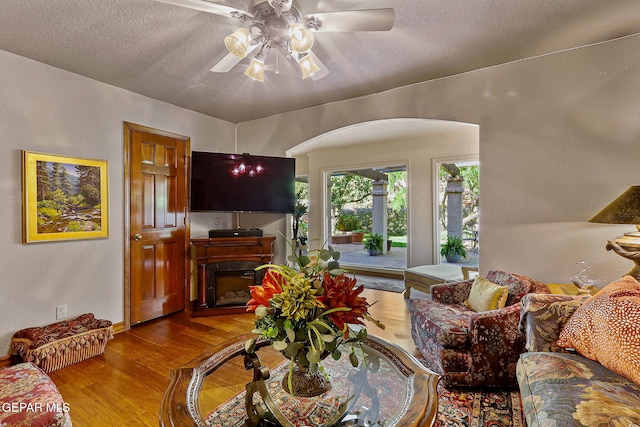 living area featuring arched walkways, a ceiling fan, wood finished floors, and a fireplace