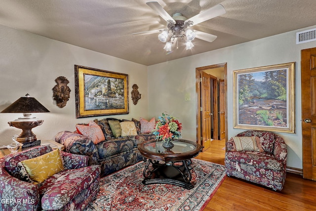 living area with visible vents, a ceiling fan, a textured ceiling, and wood finished floors