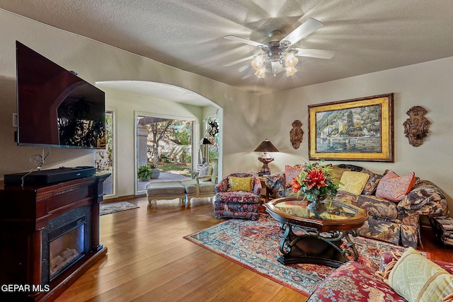 living room with arched walkways, ceiling fan, wood finished floors, and a textured ceiling
