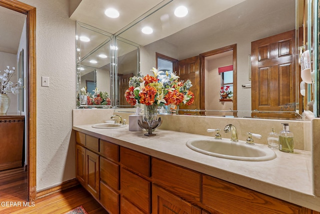 bathroom featuring double vanity, a textured wall, a sink, and wood finished floors