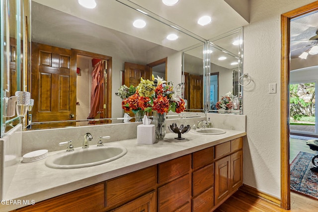 bathroom with double vanity, a textured wall, a sink, and wood finished floors