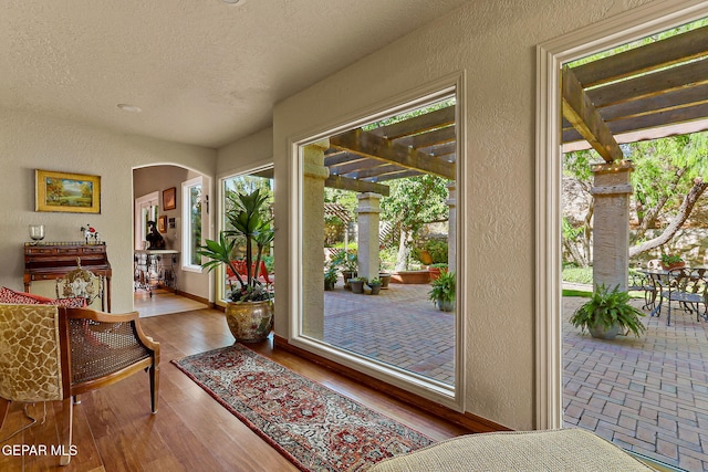 doorway to outside with a textured wall, arched walkways, a textured ceiling, baseboards, and wood finished floors