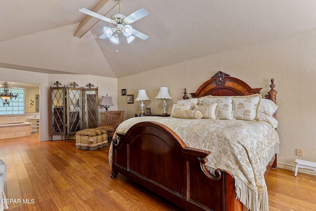 bedroom featuring a ceiling fan, wood finished floors, connected bathroom, a textured ceiling, and lofted ceiling with beams