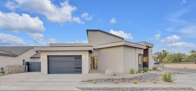 contemporary house with a garage, stucco siding, driveway, and fence
