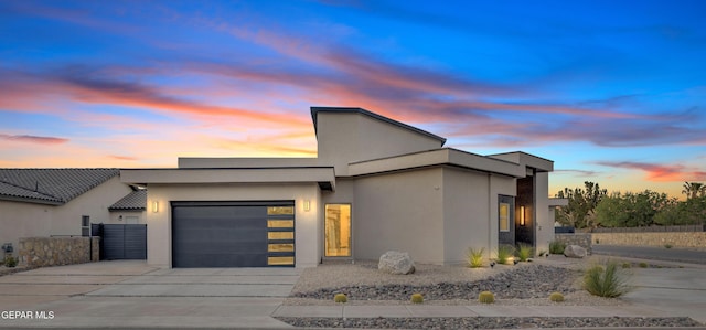 contemporary house featuring a garage, stucco siding, driveway, and fence