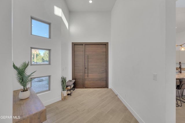 entryway featuring baseboards, recessed lighting, light wood finished floors, and a high ceiling